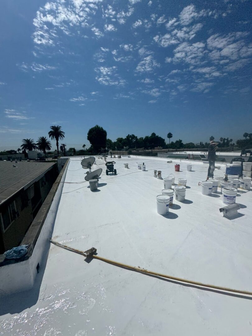 Workers installing insulation on a flat rooftop under a partly cloudy sky.