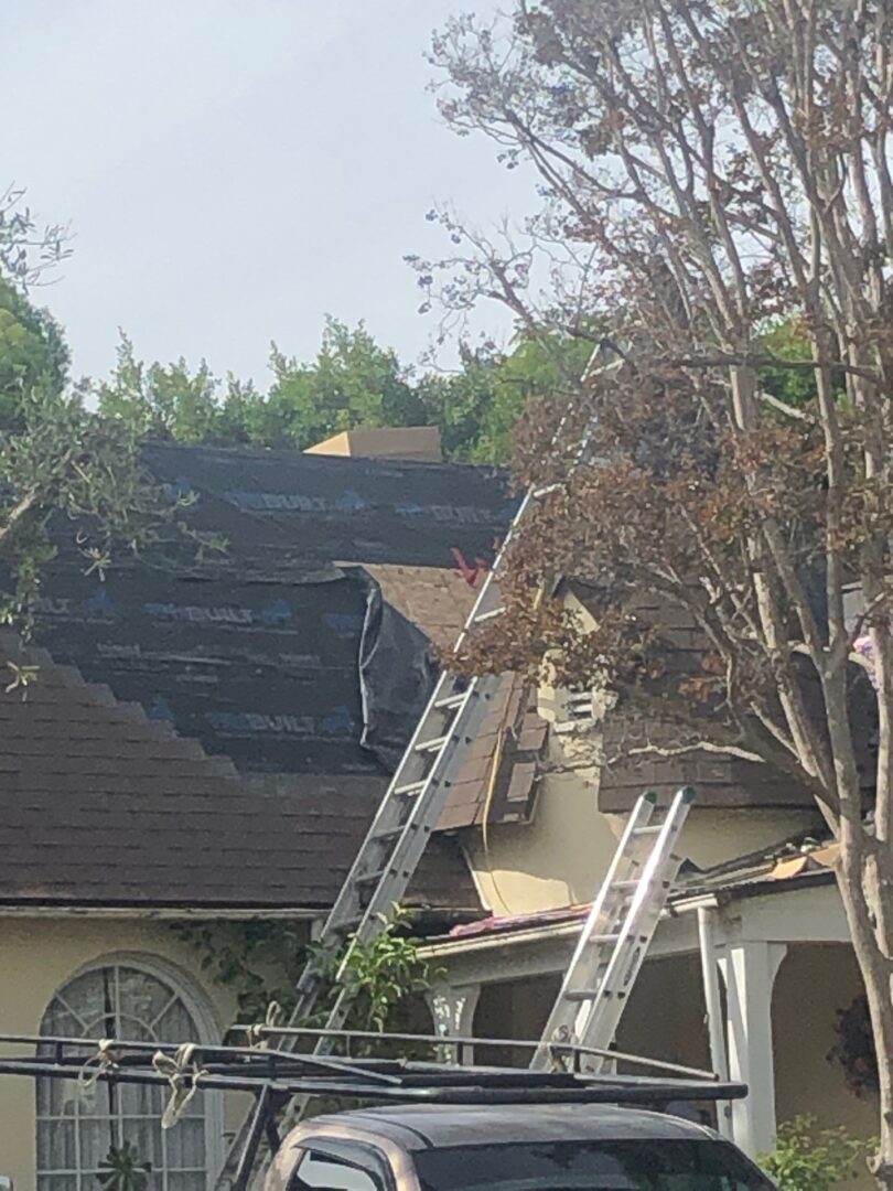Workers repairing a house roof with ladders and tools.