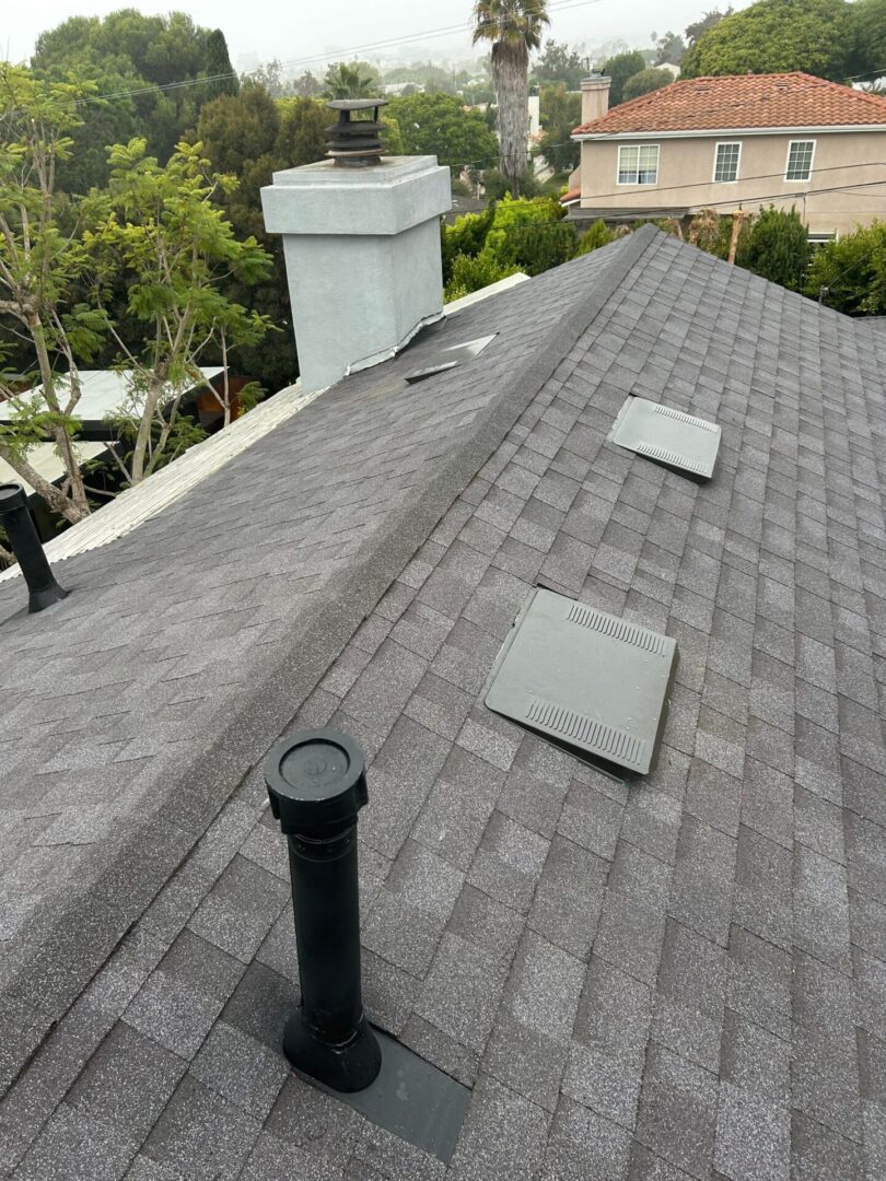A rooftop with gray shingles and ventilation pipes.