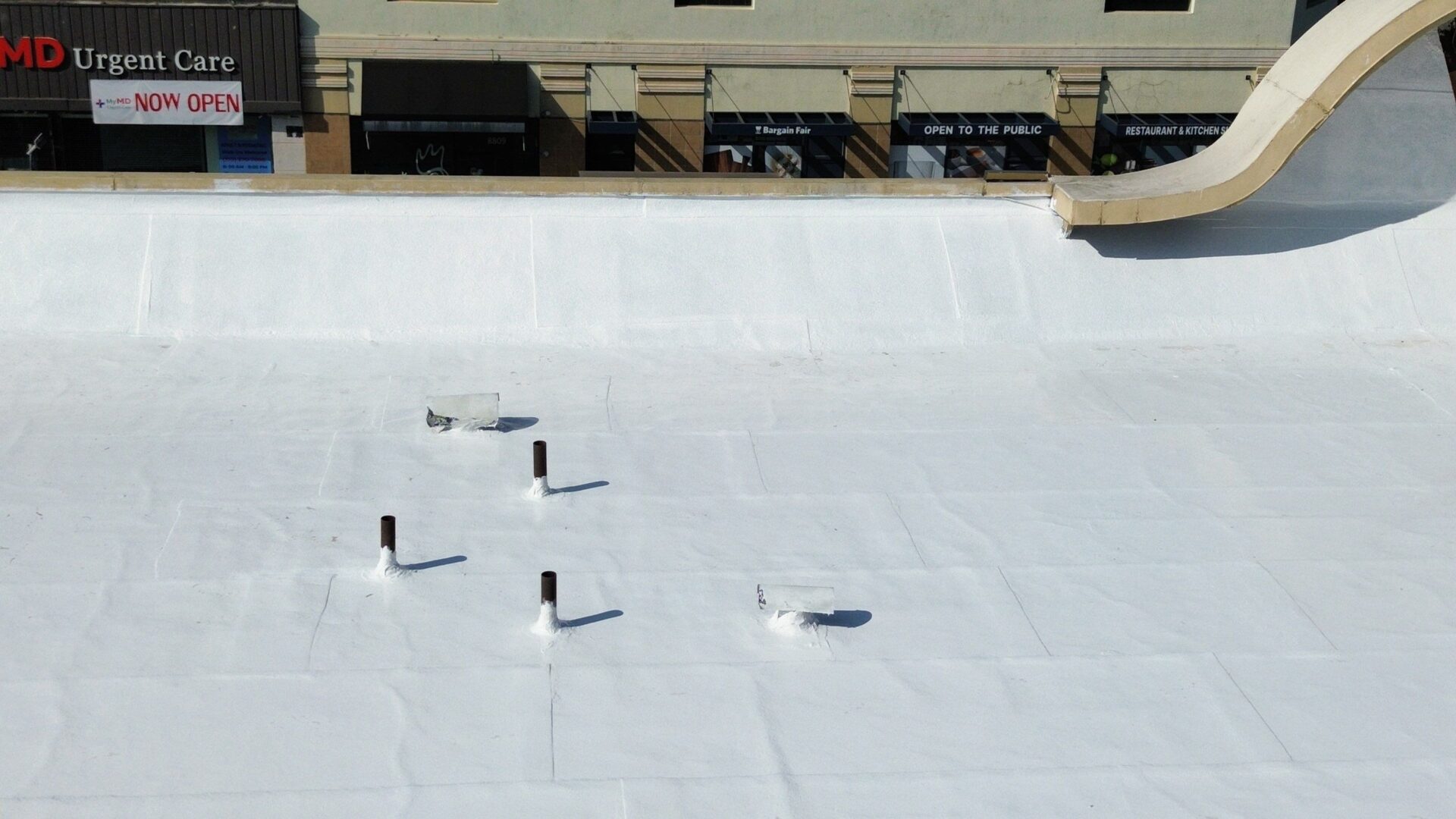 Flat rooftop with white waterproofing and vent pipes.