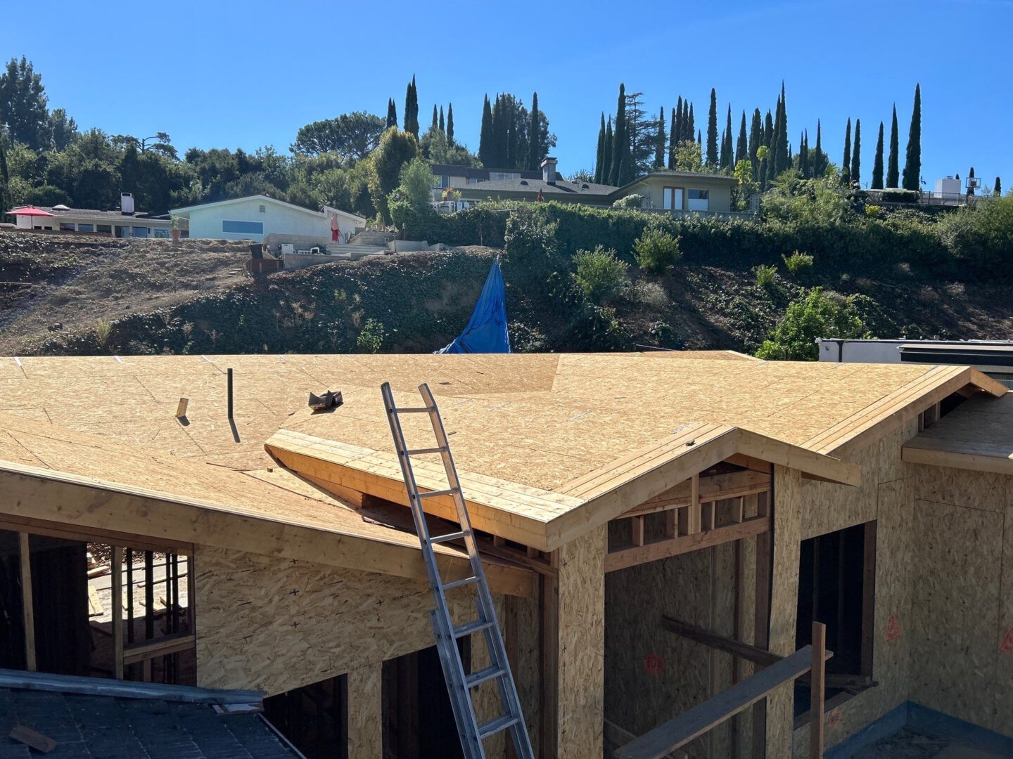 Construction workers install roofing plywood on a house under clear blue sky.