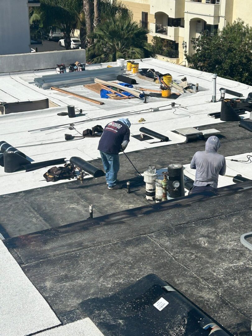 Two workers applying roofing materials on a flat roof.