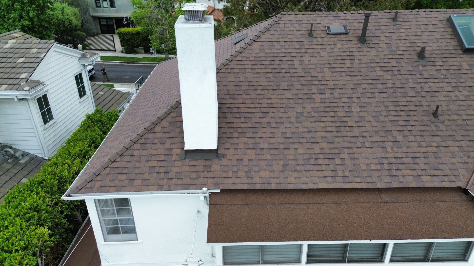 A brown shingled roof with a white chimney on a residential house.