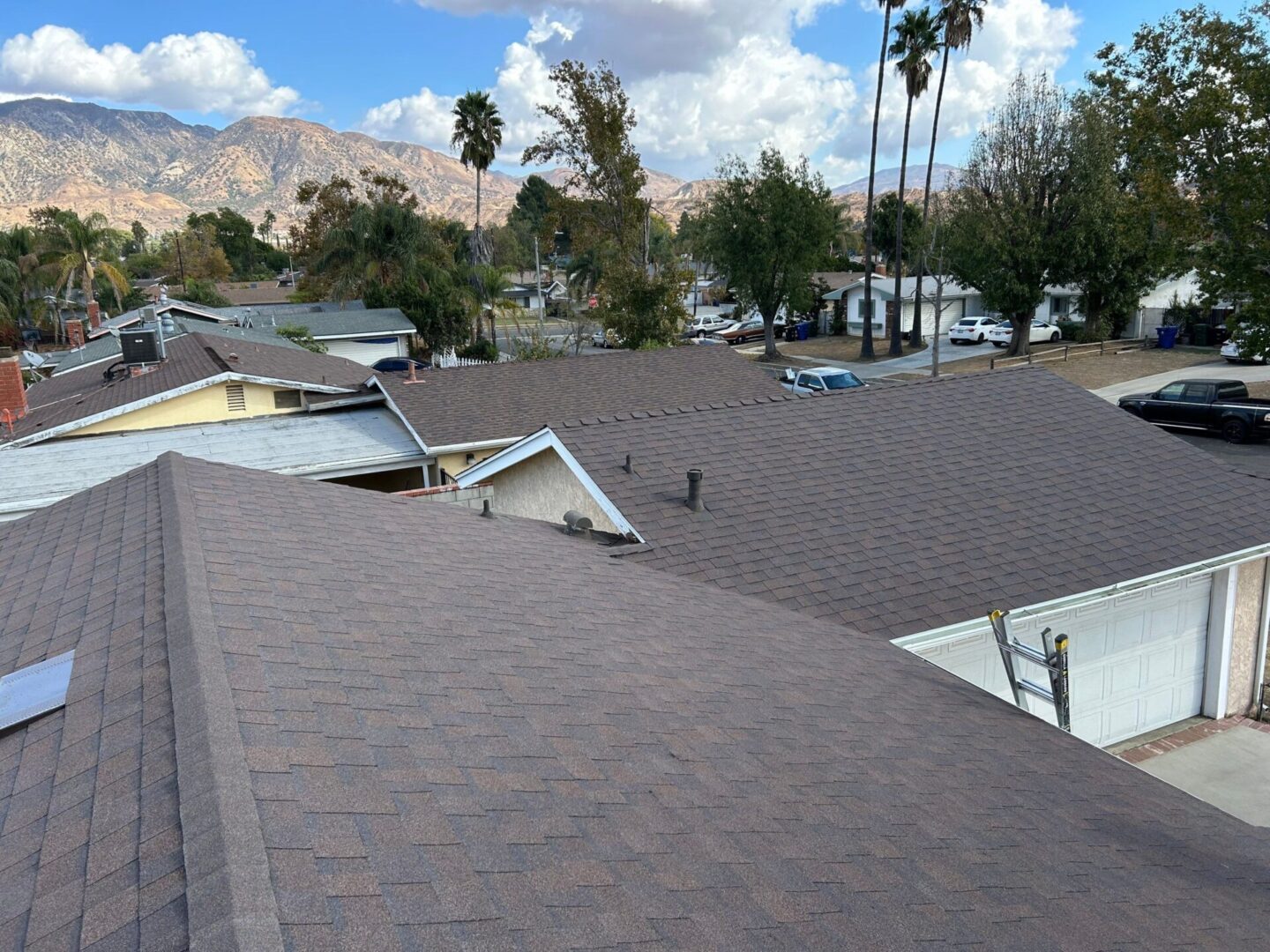 View of rooftops with brown shingles against a sunny sky and distant mountains.