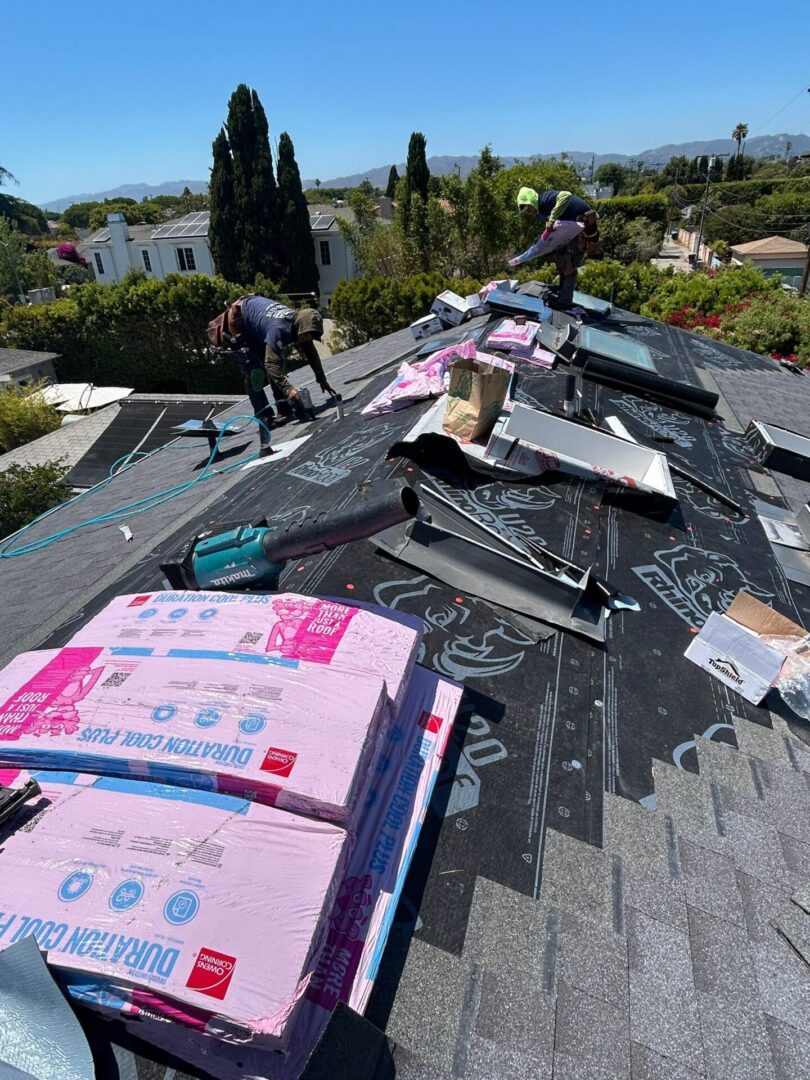 Workers installing pink insulation on a roof under a clear sky.