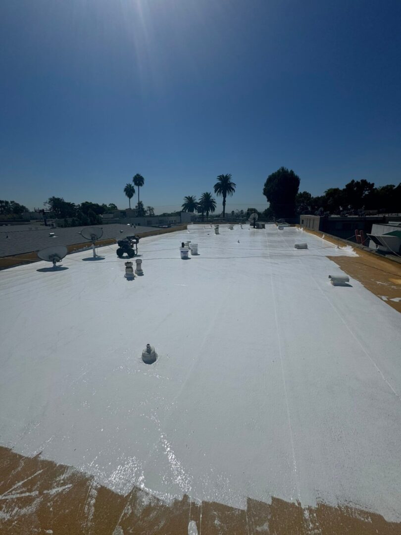 Workers installing a white waterproof membrane on a flat rooftop under clear blue sky.