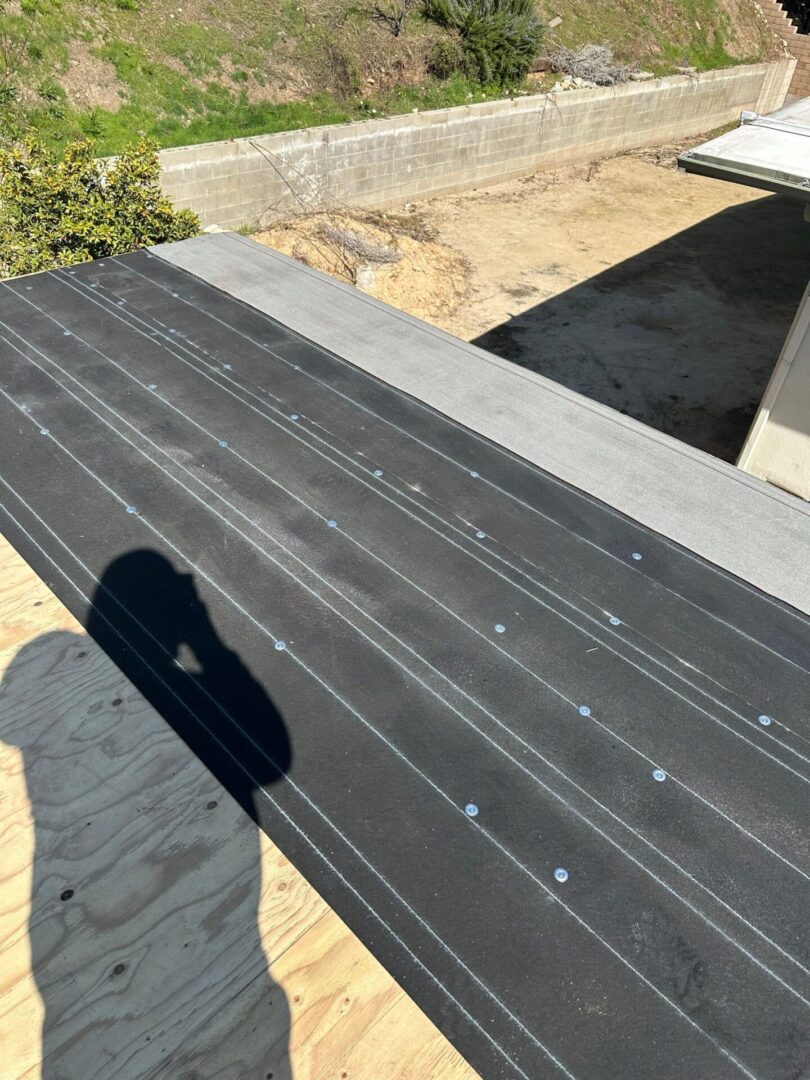 A shadow falls on a black roof under construction with screws visible.