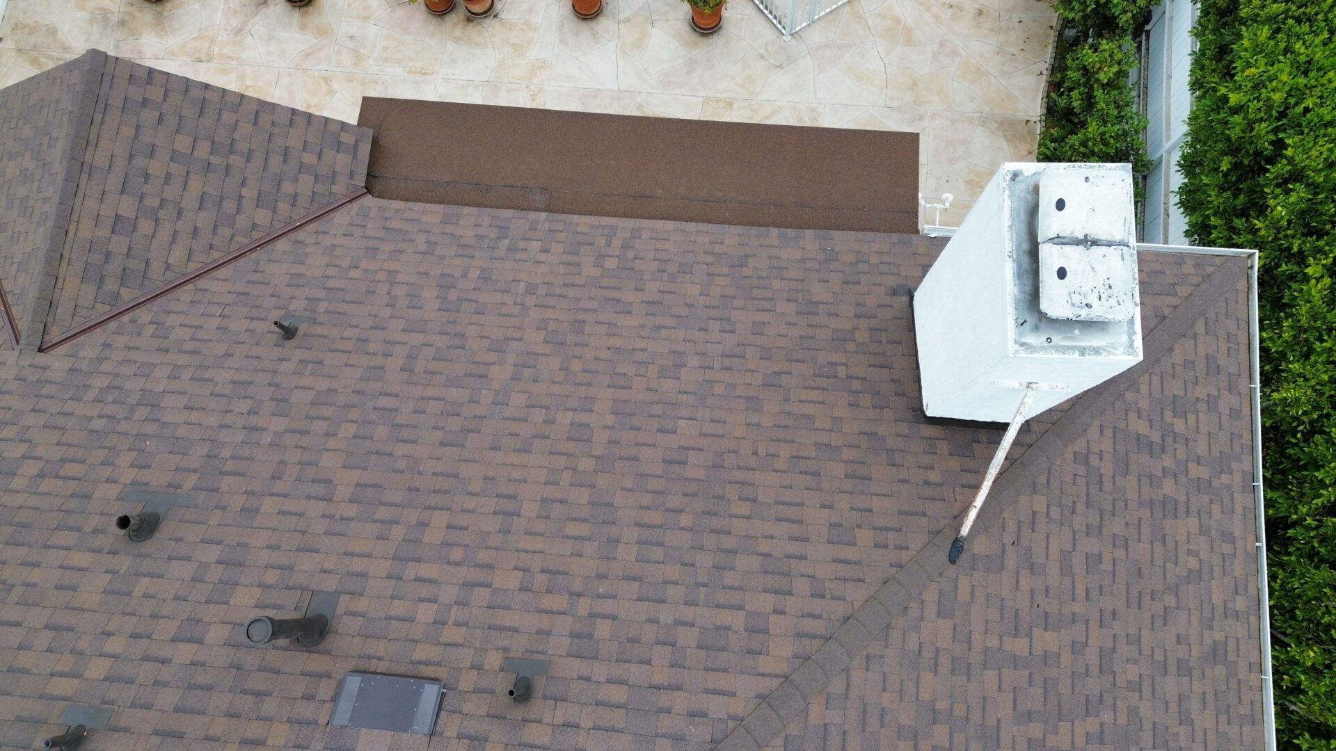 A rooftop view showing a brown shingle roof and part of an outdoor area.