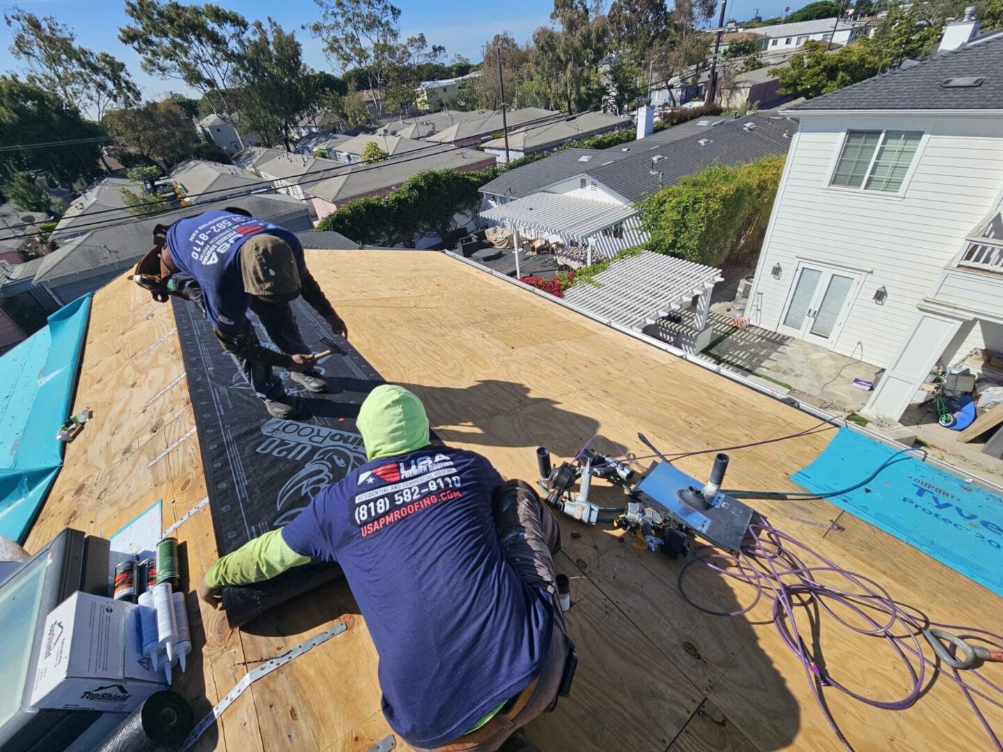 Two workers installing plywood on a residential roof under clear skies.