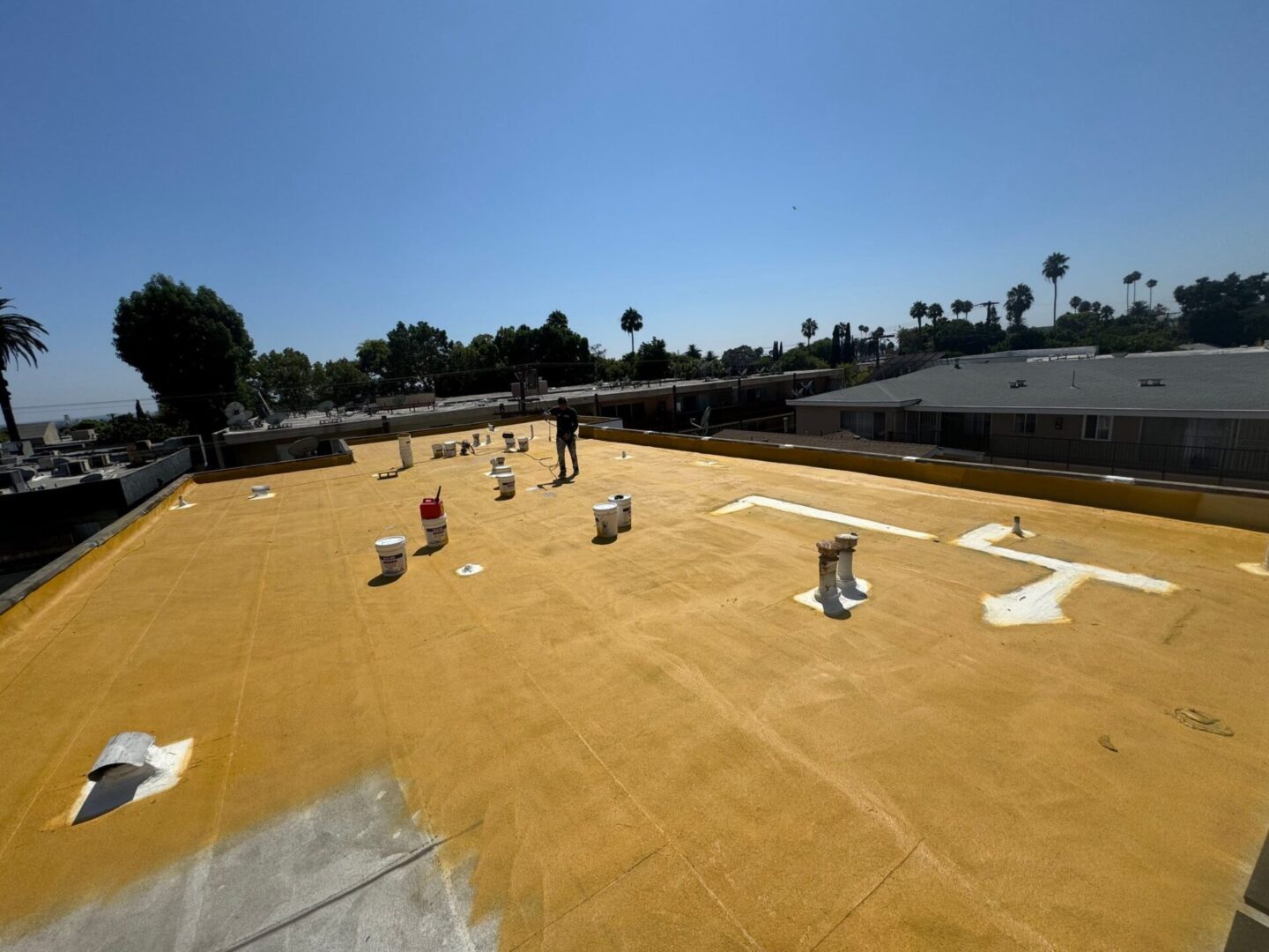 Workers preparing a large rooftop with insulation material under a clear blue sky.