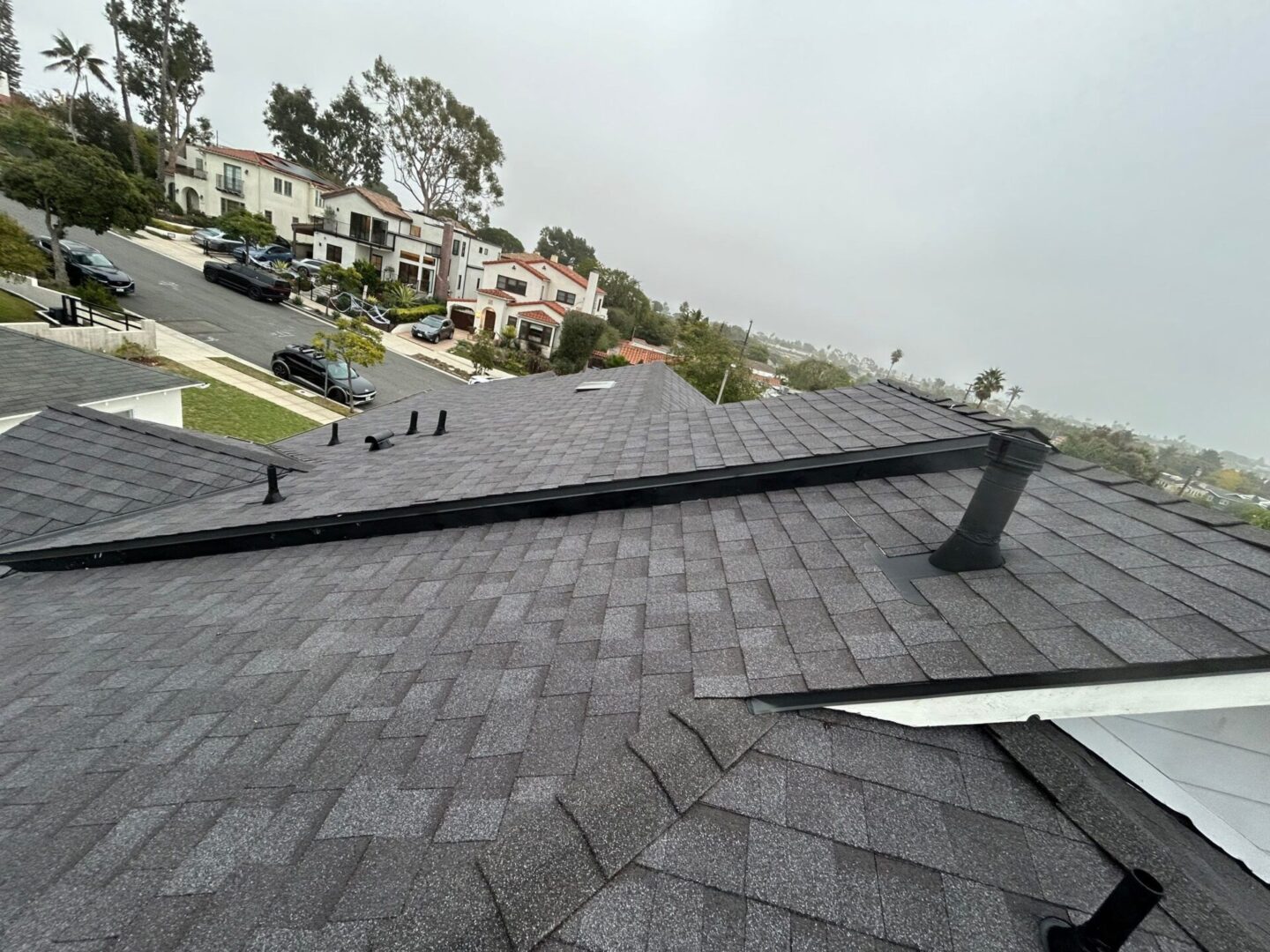 View of a shingled rooftop with nearby houses under a cloudy sky.
