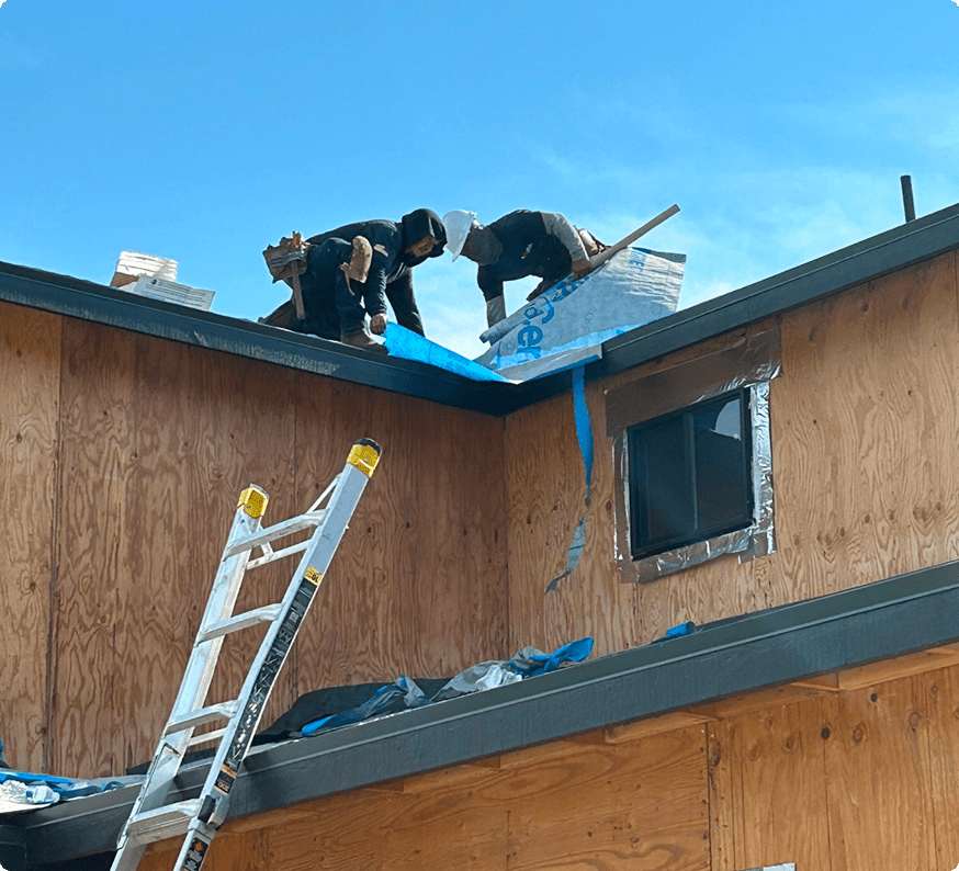 Two workers installing solar panels on a rooftop under clear skies.
