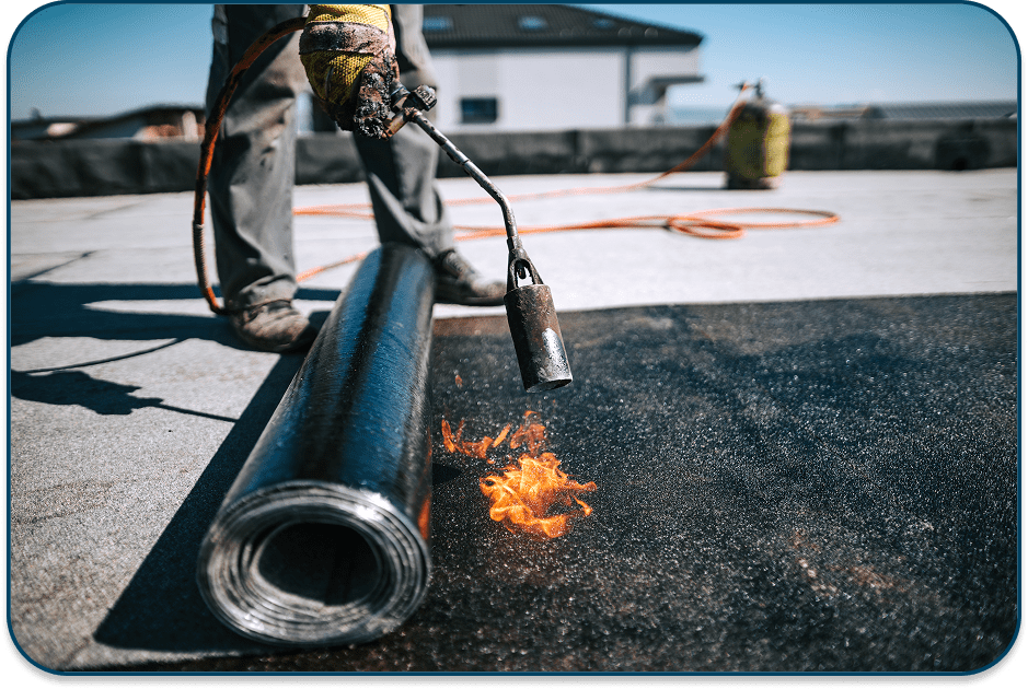 Worker applying roofing material with a torch on a flat roof.