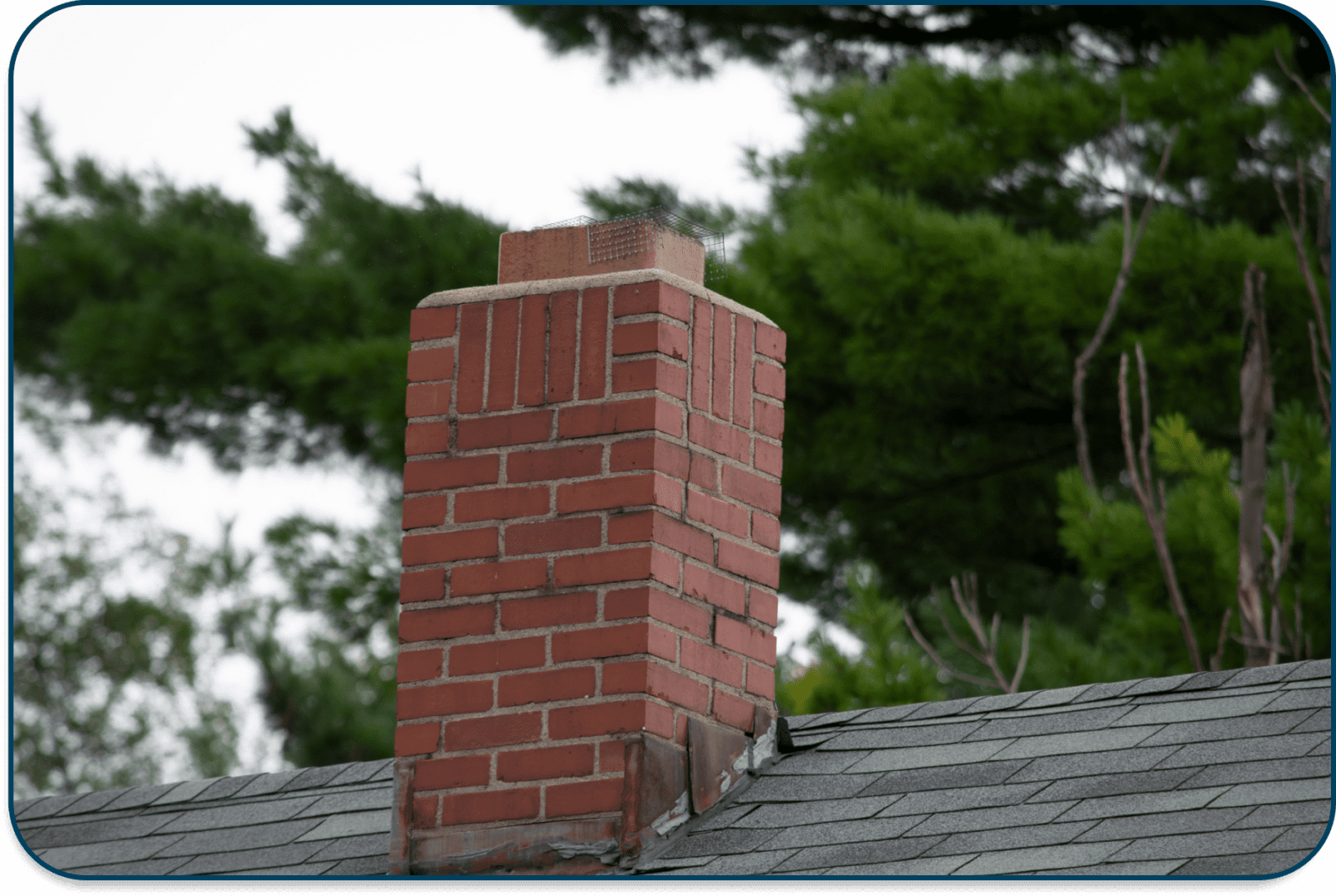 A brick chimney on a rooftop surrounded by trees.