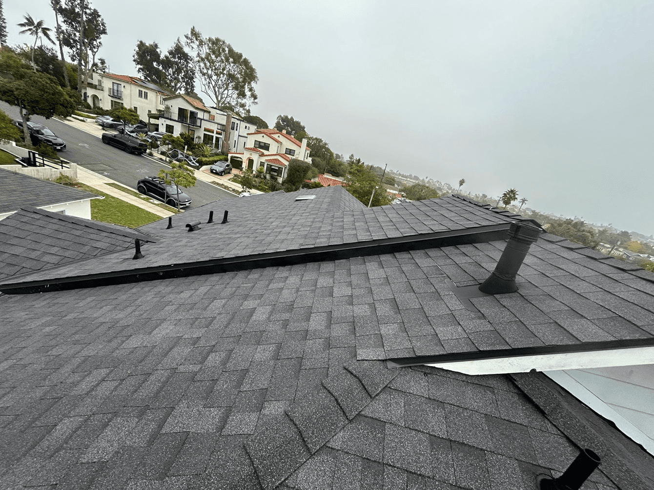 A rooftop with gray shingles overlooking a residential neighborhood.