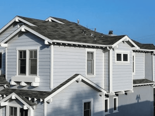 A white house with roof damage under a clear blue sky.
