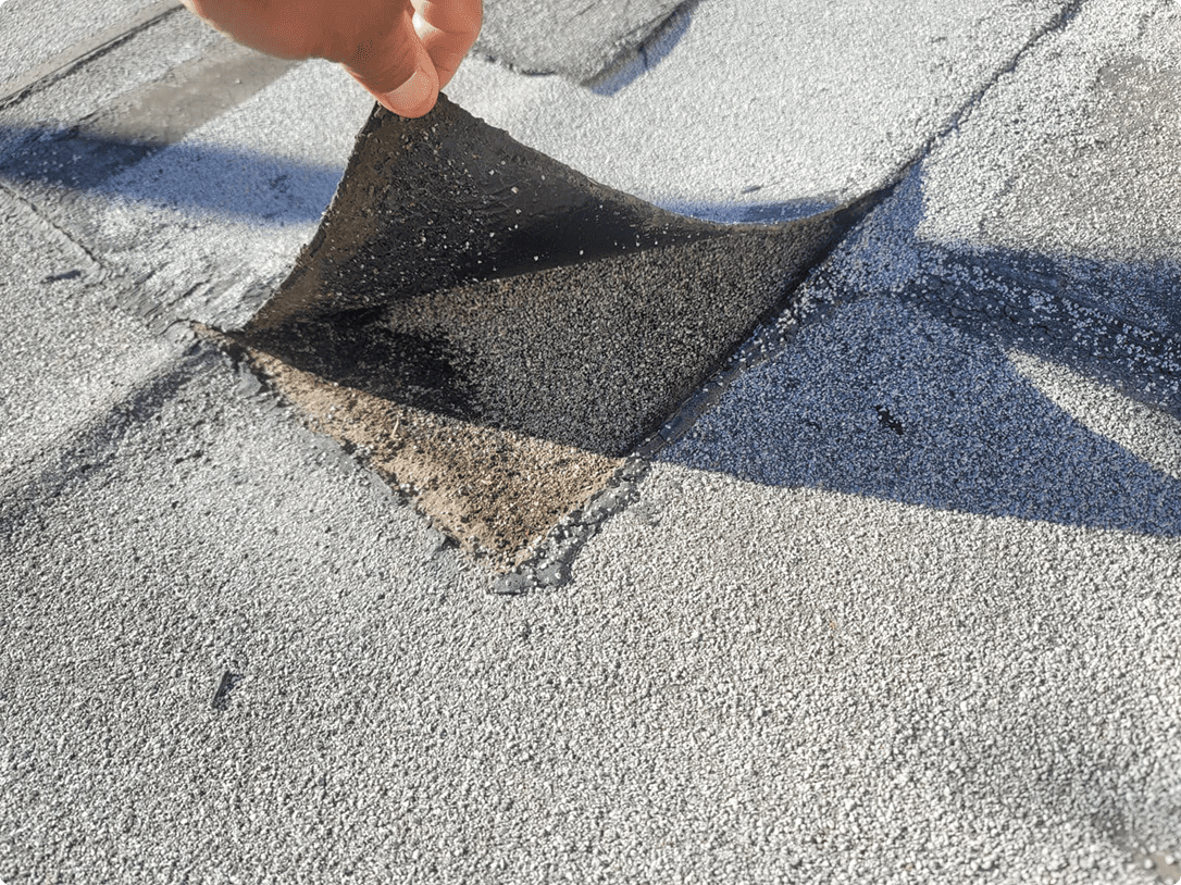A hand lifting a torn section of asphalt from a road surface.